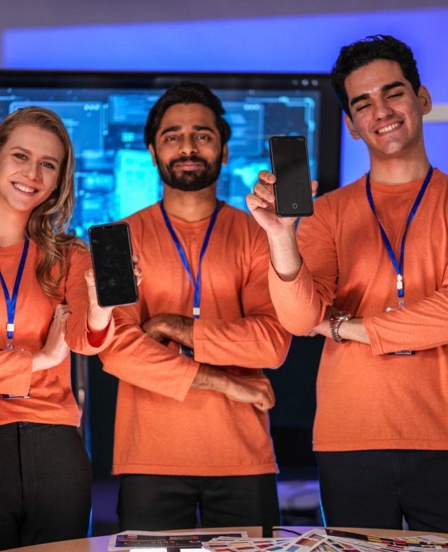 A successful, diverse team of young professionals in a modern tech company proudly presents their new mobile application, smiling confidently at the camera to celebrate a product launch.
